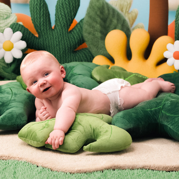 Baby lying on a green plush toy with a colorful play mat in the background