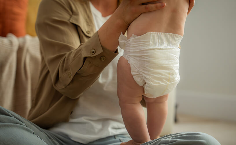 Parent holding a standing baby wearing a Dyper diaper