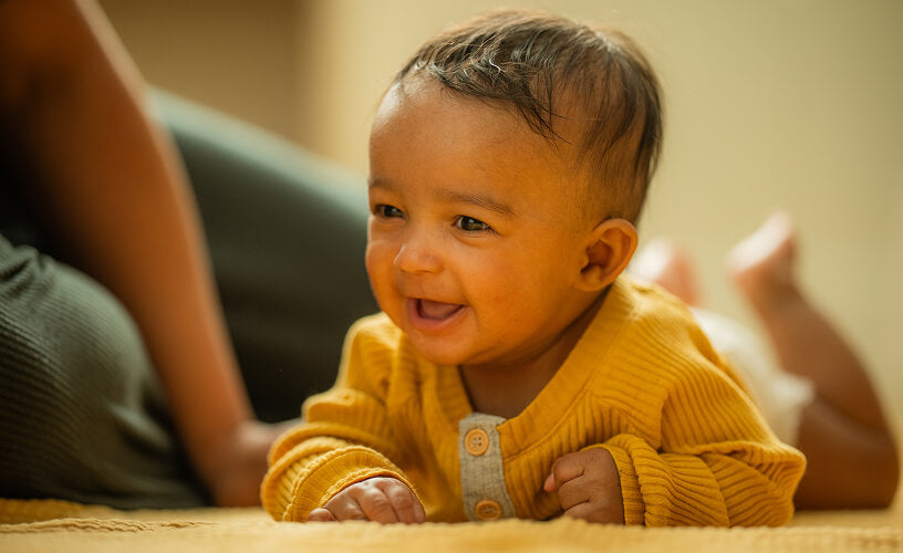 Smiling baby in a yellow cardigan lying on a rug