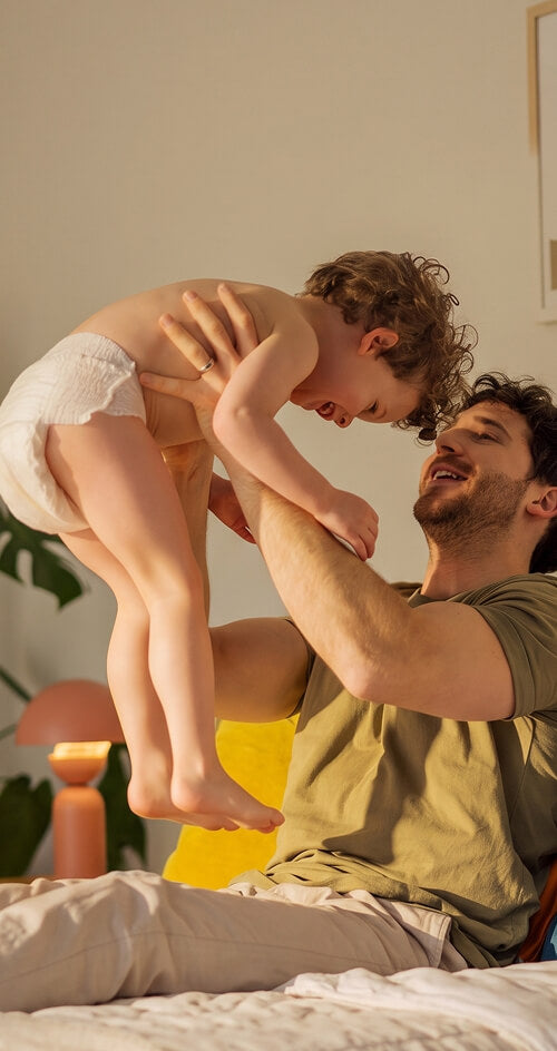 Father lifting his laughing toddler above the bed